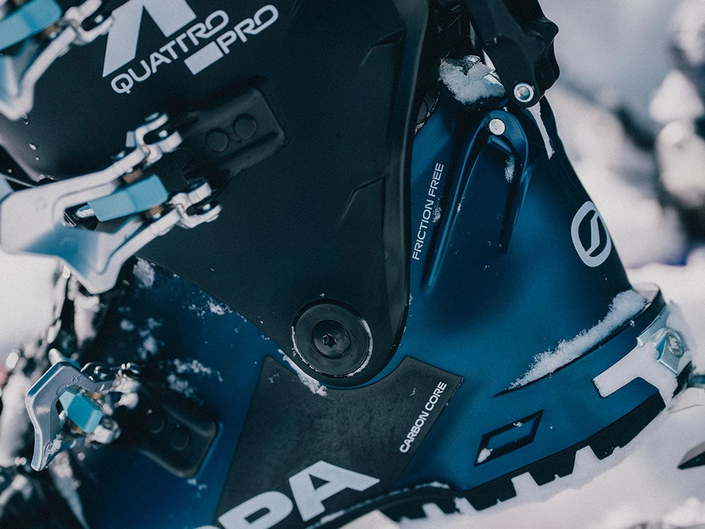 Close-up of a Scarpa ski boot in dark blue and black with snow on it, featuring the Scarpa logo and 4-Quattro Pro branding.