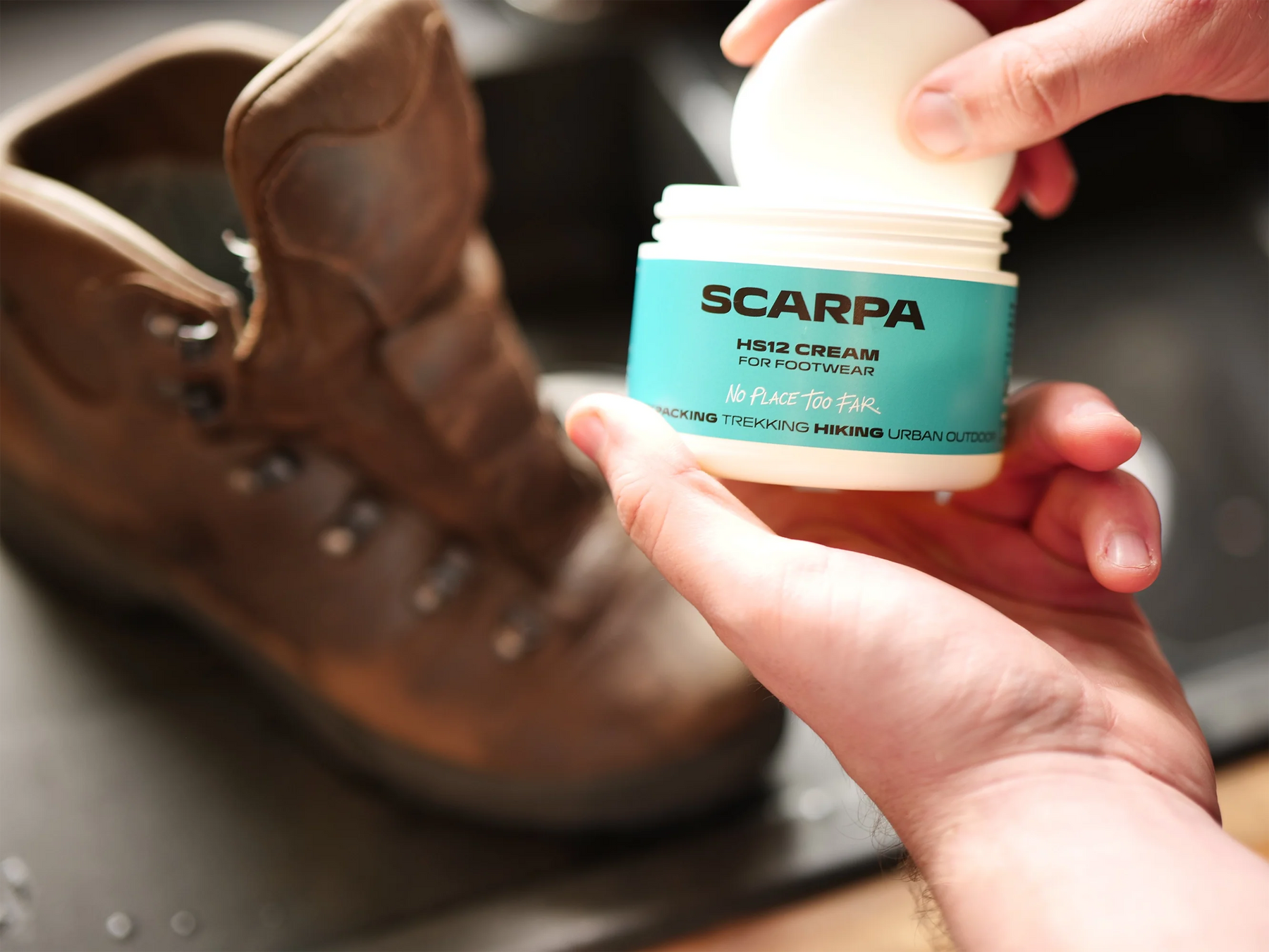 Person holding a Scarpa waterproof cream next to a brown boot